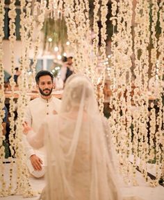 a man and woman standing in front of a wedding arch with white flowers on it