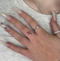 a woman's hand with white manies and tattoos on her left thumb, wearing a ring