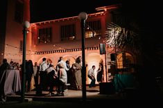 a group of people that are standing in front of a building at night with lights on