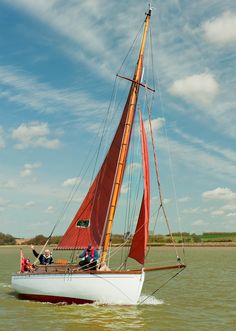 a sailboat with two people on it in the water under a blue cloudy sky