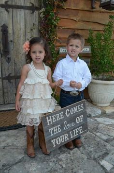 two young children standing next to each other in front of a wooden sign that says here comes the love of your life