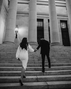 a man and woman walking up some steps holding each other's hands in black and white