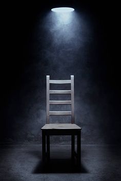 a wooden chair sitting in the dark under a light