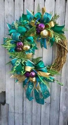 a green wreath with purple and gold ornaments on it hanging on a wooden fence next to a door