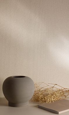 a white vase sitting on top of a table next to a book and some dried plants