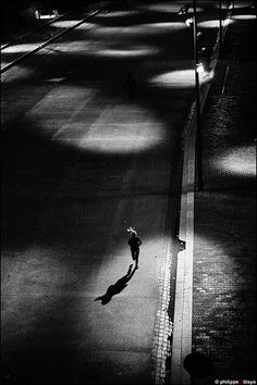 a person walking down the street at night with their shadow on the ground and one person running