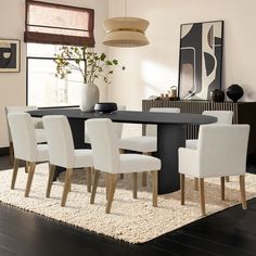 a dining room table with white chairs and a rug on the floor in front of it