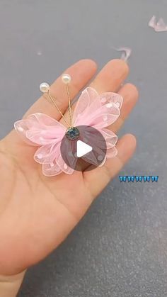 a hand holding a tiny pink flower brooch on it's thumb with a video playing button in the middle