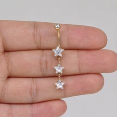 a person is holding a gold and diamond star belly ring in their left hand, while the other one has three diamonds on it