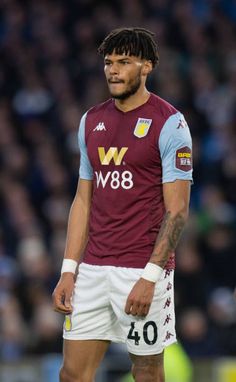 a man with dreadlocks standing on a soccer field wearing a maroon and white uniform