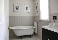 a white bath tub sitting in a bathroom next to a sink and window with pictures on the wall