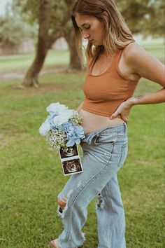 a pregnant woman holding a bouquet of flowers in her stomach while standing on the grass