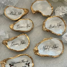 some white and gold oysters with names on them sitting on a lace covered tablecloth