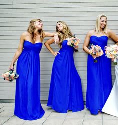 three women in blue dresses standing next to each other and one is holding her bouquet