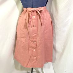 Vintage 80's pink midi skirt. The skirt is unbranded. It sits at the natural waist and has a gentle a line fit. The skirt buttons all they way down the front. It has two large side pockets. The skirt has a matching fabric belt. There is no fabric content tag but it feels like a lightweight polyester.  In very good vintage condition.  There are no size tags.  Measurements  Waist - 27 inches  Hip- 42 inches  Length- 25.5 inches Pink High Waist Skirt For Workwear, High Waist Pink Skirt For Work, Pink High Waist Skirt For Work, Pink High Waist Lined Pencil Skirt, High Waist Pink Pencil Skirt With Lining, Long Pink Pencil Skirt For Spring, Relaxed Pink Skirt For Daywear, Pink Lined Skirt For Daywear, Pink Long Skirt For Daywear