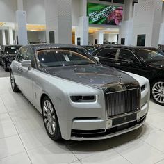 two rolls royces are on display in a showroom, one is silver and the other is black