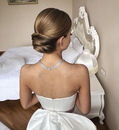 a woman in a white dress sitting on a bed with her back to the camera