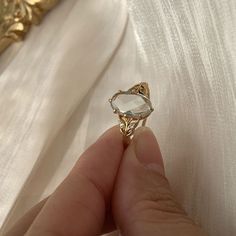 a person holding a ring in their hand on a white cloth with gold trimmings