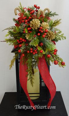 a christmas arrangement with pine cones, berries and greenery in a black vase on a table