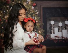 a woman holding a baby in front of a christmas tree