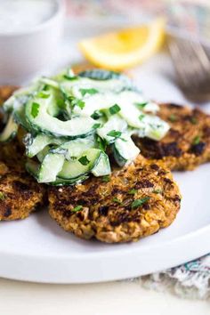 a white plate topped with crab cakes covered in cucumber and green onions next to a fork