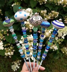 a hand holding several glass objects in front of some white and blue flowers with green leaves