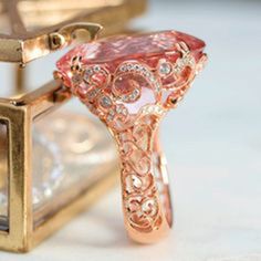 a pink diamond ring sitting on top of a white table next to a gold box