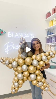 a woman holding up a star shaped balloon in front of a store display with gold and silver balloons