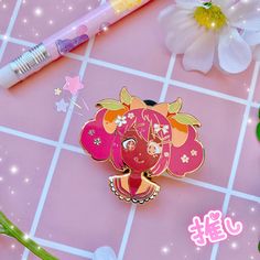 an elephant pin sitting on top of a pink table next to flowers and a pen