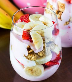 two glasses filled with fruit and yogurt on top of a table next to bananas