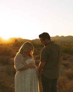 a pregnant couple standing in the desert at sunset