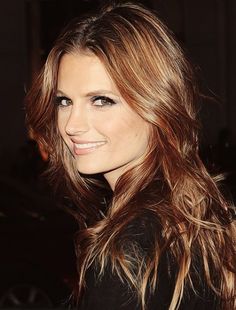 a woman with long brown hair and blue eyes smiles at the camera while standing in front of a car