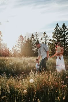 a man and woman holding hands walking through tall grass with trees in the back ground