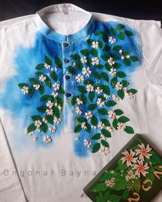 a shirt with flowers painted on it next to a book