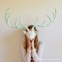 a woman covering her face with a fake deer's antlers on top of her head