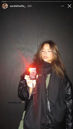 a woman taking a selfie with her camera in front of a black wall at night