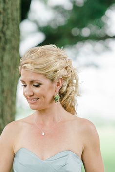 a woman standing next to a tree wearing a strapless dress and green earrings on her head