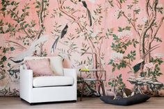 a living room with pink wallpaper and birds on the tree branches, in front of a white chair