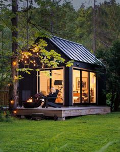 a small black cabin in the woods with lights on