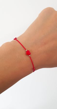 a woman's arm wearing a red string bracelet with two hearts on the clasp