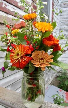 a mason jar filled with lots of flowers on top of a wooden table next to a house