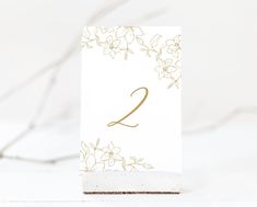 a white table number with gold flowers on it and the number two written in gold