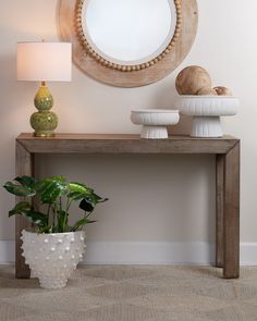 a wooden table with two white vases and a mirror on the wall behind it