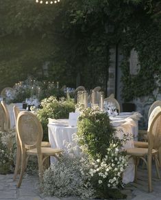 an outdoor dining area with tables and chairs covered in white linens, surrounded by greenery