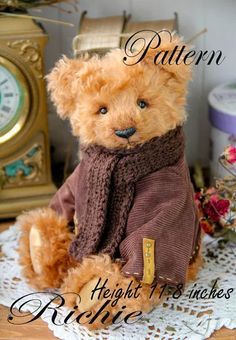 a teddy bear wearing a sweater and scarf sitting on a doily next to a clock