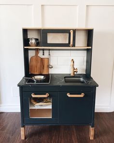 a toy kitchen with black cabinets and wooden floors, including a sink and countertop