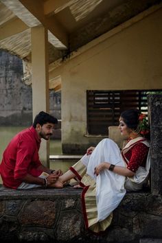 a man and woman sitting next to each other on a stone wall in front of a building