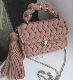 a pink handbag sitting on top of a white table next to a chain necklace