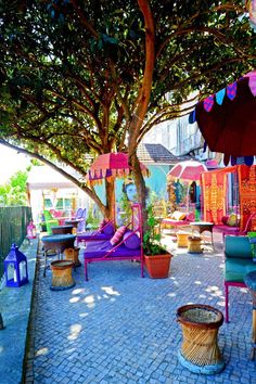 an outdoor area with colorful furniture and umbrellas on the patio, next to a tree