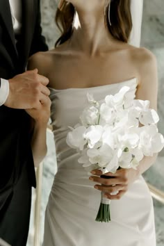 a bride and groom standing next to each other in front of a mirror holding white flowers